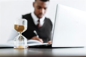 Person working at a laptop, with an hour glass on the desk.