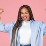 A feminine presenting Black professional flexing their biceps for International Women's Day 2025 theme, #AccelerateAction