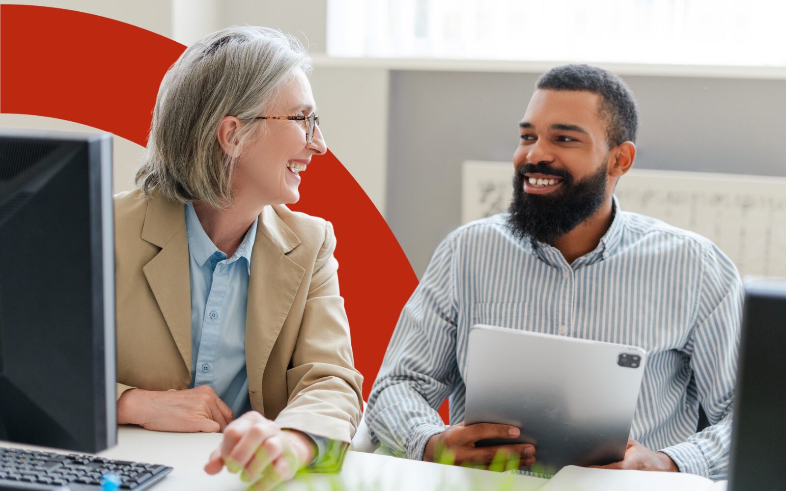 An image of two men sitting at a table smiling at each other. On the table are notes and a laptop. They are both wearing smart casual outfits.