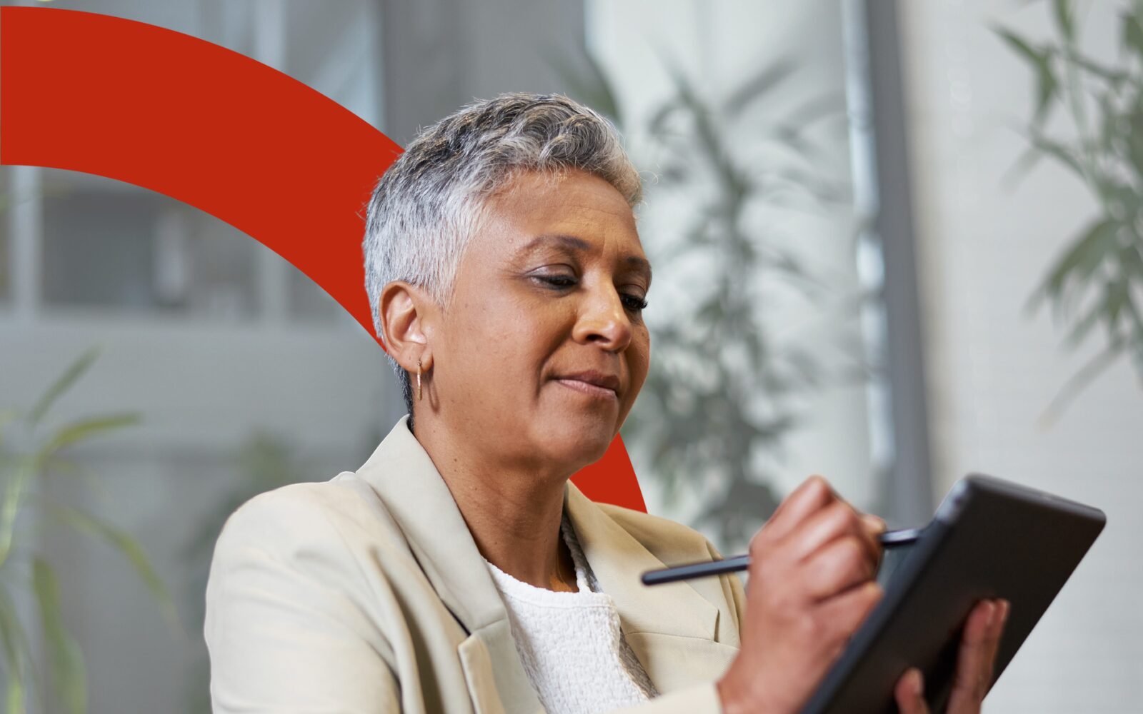Photo of a women writing on her tablet. She has silver hair and is wearing a cream suit.
