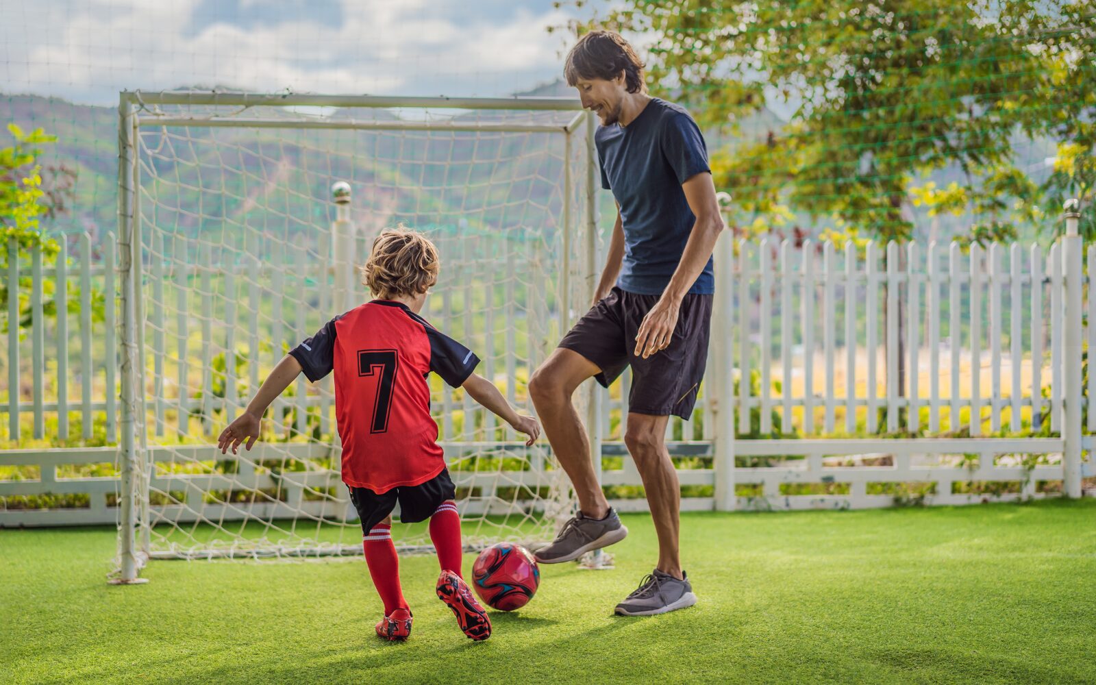 A parent and child playing football together on a football pitch
