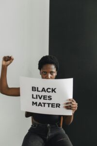 Photo of a Black woman holding her fist in the air and holding a signs saying Black Lives Matter.