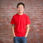 A football fan wearing a red t shirt to support Wear Red Day. They are smiling and standing in front of a brick wall.